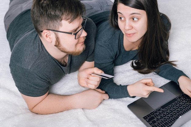 Couple on a bed with a laptop and card discussing whether spousal Social Security benefits can be claimed before a partner files
