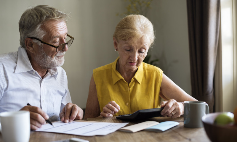 Senior couple reviewing financial documents with a calculator at a dining table, learning how to avoid double taxation on rollovers