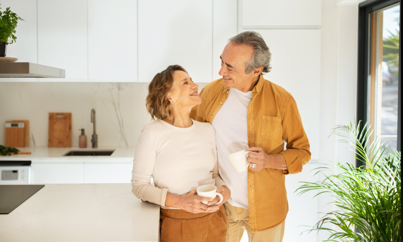 Older couple smiling over coffee in a modern kitchen, enjoying the lifestyle they want to protect before retiring