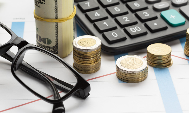 Stacked coins beside a calculator and rolled banknote, illustrating how investment fees quietly erode retirement savings