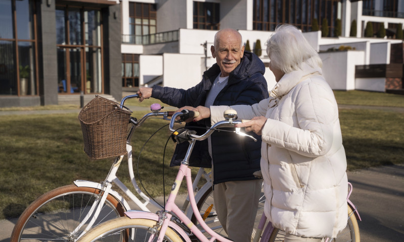 Senior couple with bicycles outside a modern building on a sunny day, finding the best small towns to retire in 2025