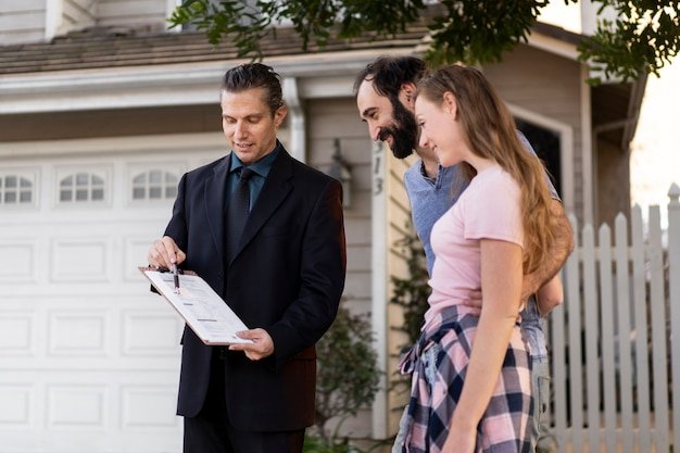Professional reviewing documents with a couple outside a suburban house, helping them choose a trustworthy executor for their estate