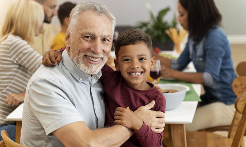 Grandfather hugging a smiling grandson at a family dinner table, illustrating how to claim Social Security for dependent children