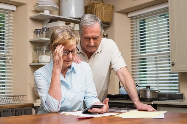 Older couple looking stressed over financial documents and a calculator, facing common retirement planning mistakes