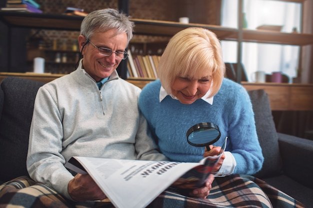 Senior couple on a sofa reading a document with a magnifying glass, studying real early retirement case studies for planning inspiration