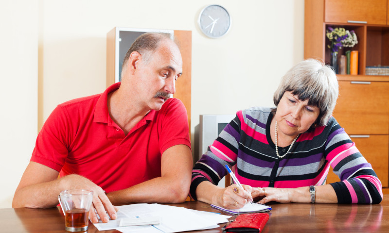 Older couple at a home table reviewing tax documents, woman signing paperwork while planning how to handle taxes before 65