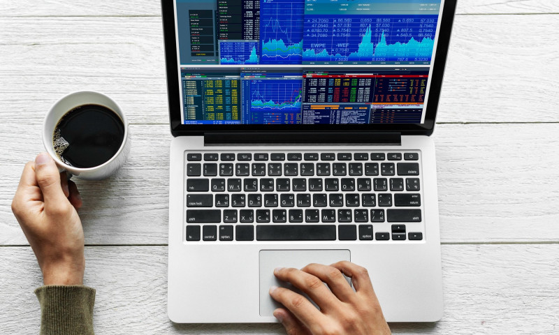 Person watching stock charts on a laptop with coffee, deciding how often to rebalance a retirement portfolio