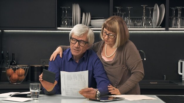 Older couple reviewing printed financial documents at a kitchen counter, understanding how retirement income is taxed