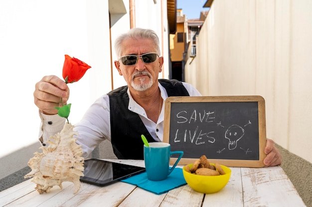 Confident older man with sunglasses holding a red rose at an outdoor table, enjoying the freedom of having retired at 50