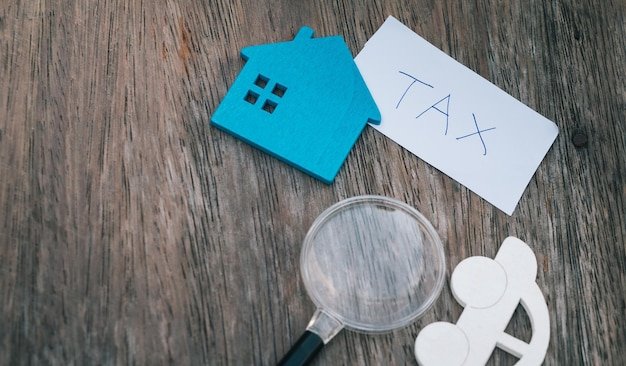 Small blue house figurine next to a TAX card and a magnifying glass, comparing inheritance tax and estate tax obligations for heirs