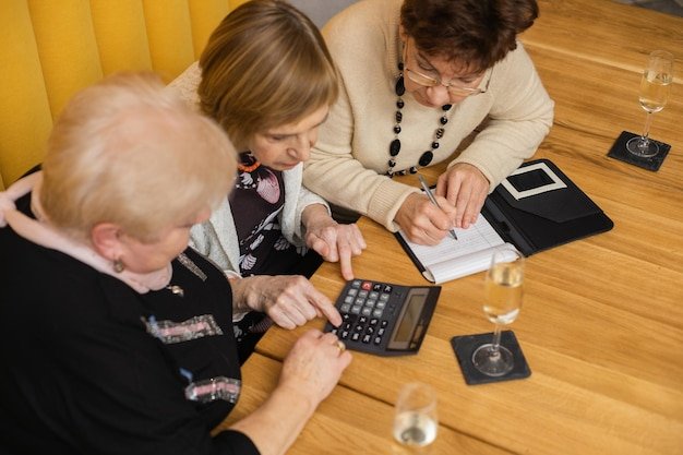 Three senior women at a table using a calculator and writing notes, calculating how to minimize taxes on Social Security benefits