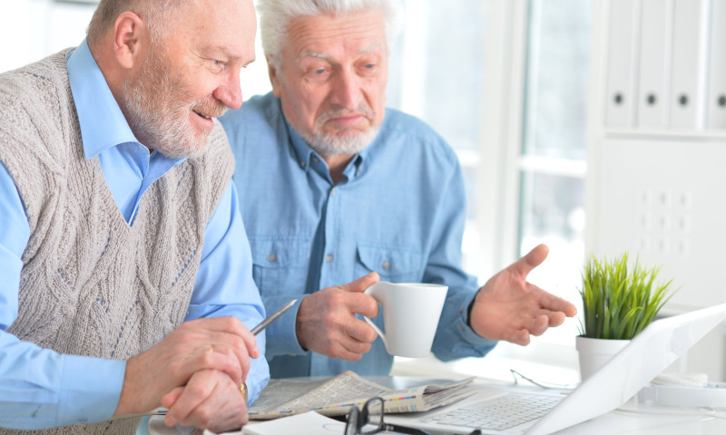 Two older men reviewing annuity documents at a desk, discussing the pros and cons for retirement income