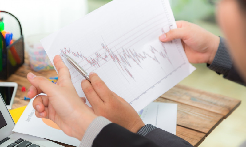 Hands holding a stock chart over a laptop, preparing a retirement portfolio defense strategy against recession