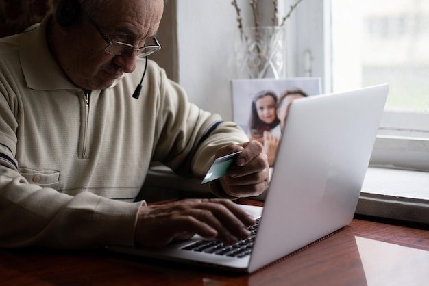 Older man with glasses using a laptop and credit card near a window, learning how to protect retirement accounts from fraud
