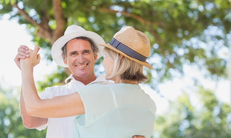 Middle-aged couple dancing outdoors in straw hats, celebrating the financial independence they achieved through FIRE