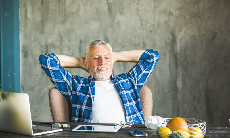 Relaxed older man leaning back at a desk with a laptop, enjoying the structured free time he created after leaving work early