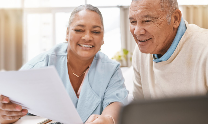 Smiling senior couple reviewing financial paperwork with a calculator, understanding required beginning dates for RMDs