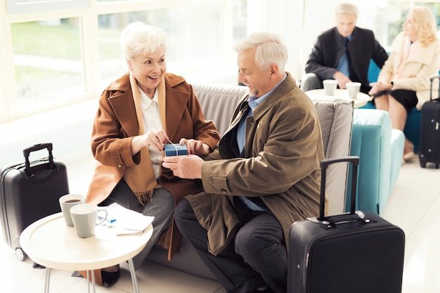 Senior couple exchanging a gift box in a bright waiting area, navigating visas and residency for retiring abroad