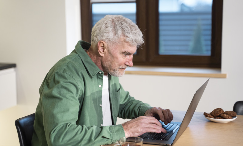 Older man working on a laptop at a kitchen table, carefully rolling over a 401k without triggering tax penalties