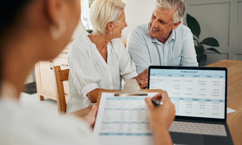 Older couple smiling at a financial review with an advisor and a budget spreadsheet, showing signs of retirement readiness