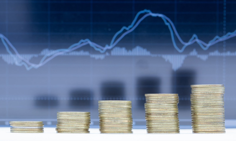 Five growing coin stacks in front of a market chart, representing investments converted into retirement income streams