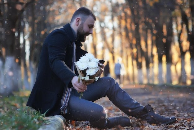 Man in a dark coat sitting alone in an autumn park holding white flowers, representing what happens to Social Security after death