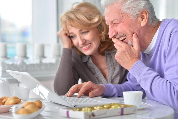 Senior couple laughing over a laptop at a dining table while researching long-term care costs