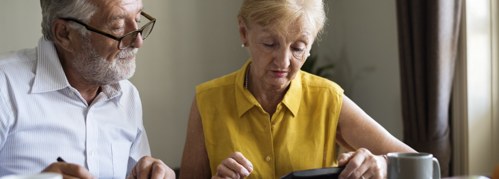 Senior couple reviewing financial documents with a calculator at a dining table, learning how to avoid double taxation on rollovers
