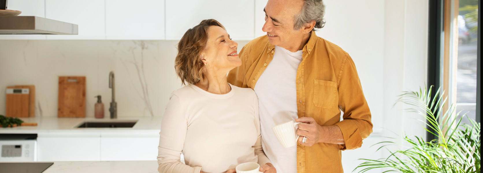 Older couple smiling over coffee in a modern kitchen, enjoying the lifestyle they want to protect before retiring