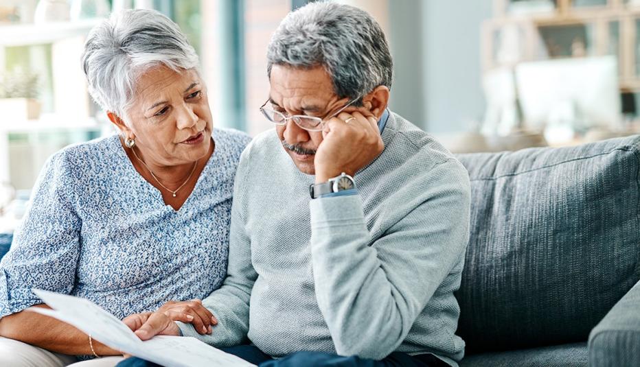 Worried older couple reviews paperwork on a couch, stressed about avoiding the Medicare late enrollment penalty
