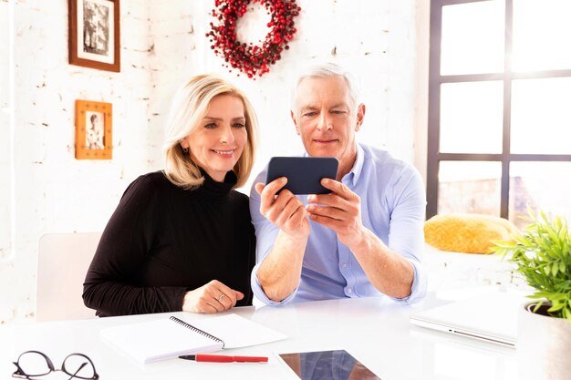 Senior couple smiling at a smartphone together, discovering the best apps to track their retirement accounts