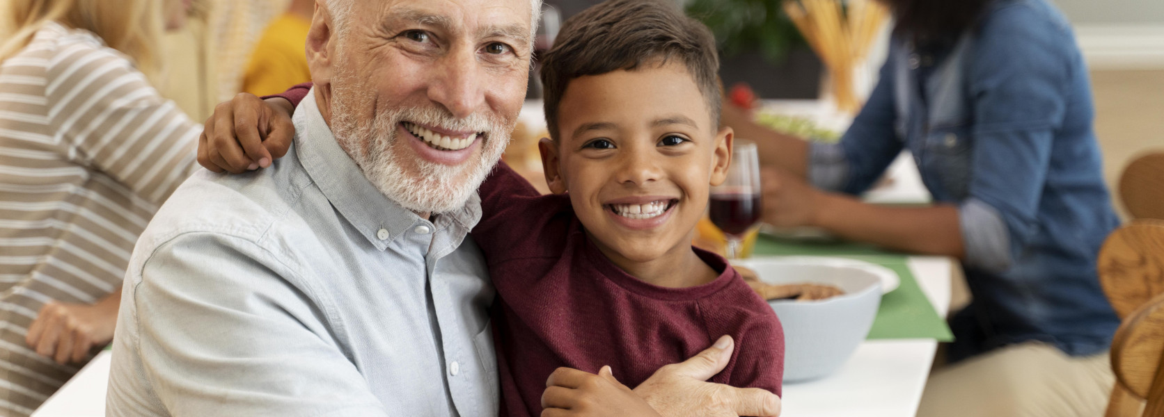 Grandfather hugging a smiling grandson at a family dinner table, illustrating how to claim Social Security for dependent children
