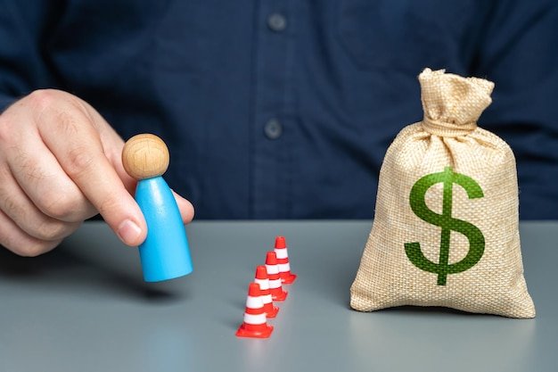 Hand placing a figurine beside traffic cones and a money bag, representing deliberate steps to cut expenses toward financial independence