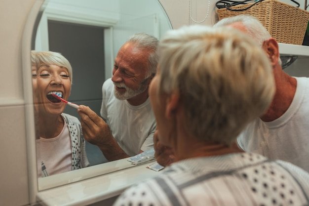 Senior man and woman smiling in a bathroom mirror while discussing dental and vision coverage in retirement
