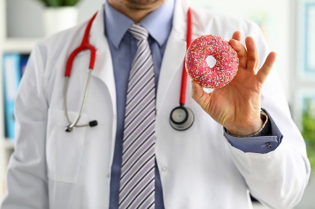 Doctor in white coat holding up a pink frosted donut with sprinkles, illustrating the Medicare donut hole