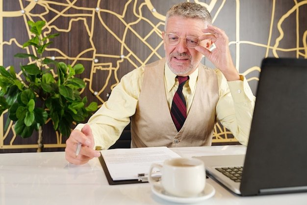 Older gentleman in suit reviewing paperwork at a desk with a laptop, finding a part-time job after retirement