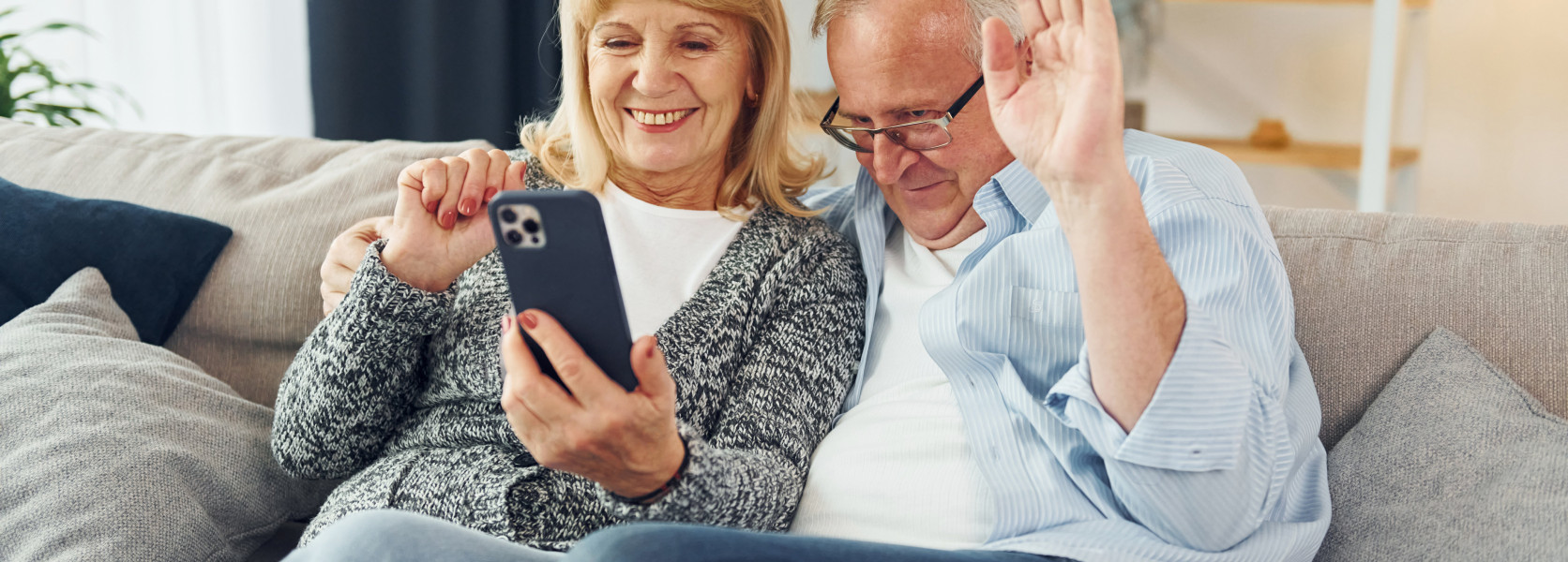 Senior couple smiling and waving at a video call on a smartphone, managing family expectations when relocating
