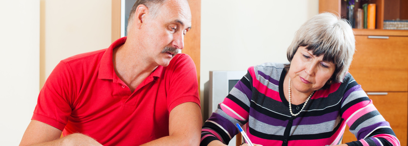 Older couple at a home table reviewing tax documents, woman signing paperwork while planning how to handle taxes before 65