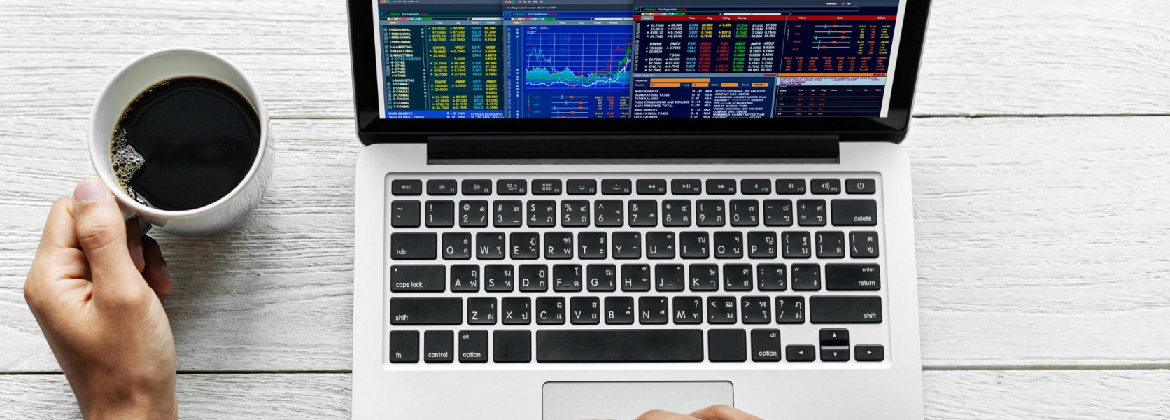 Person watching stock charts on a laptop with coffee, deciding how often to rebalance a retirement portfolio