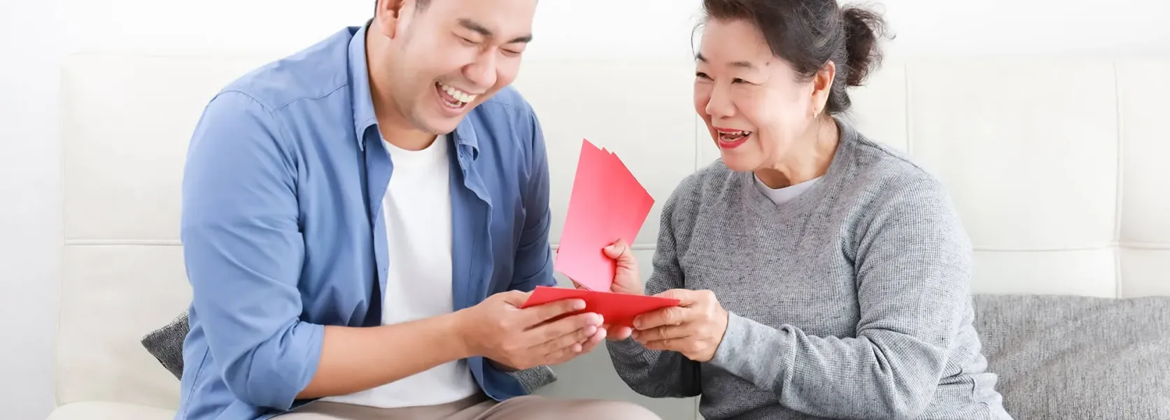 Smiling mother giving her adult son a red gift card on a sofa, illustrating how retirees legally gift money to family members