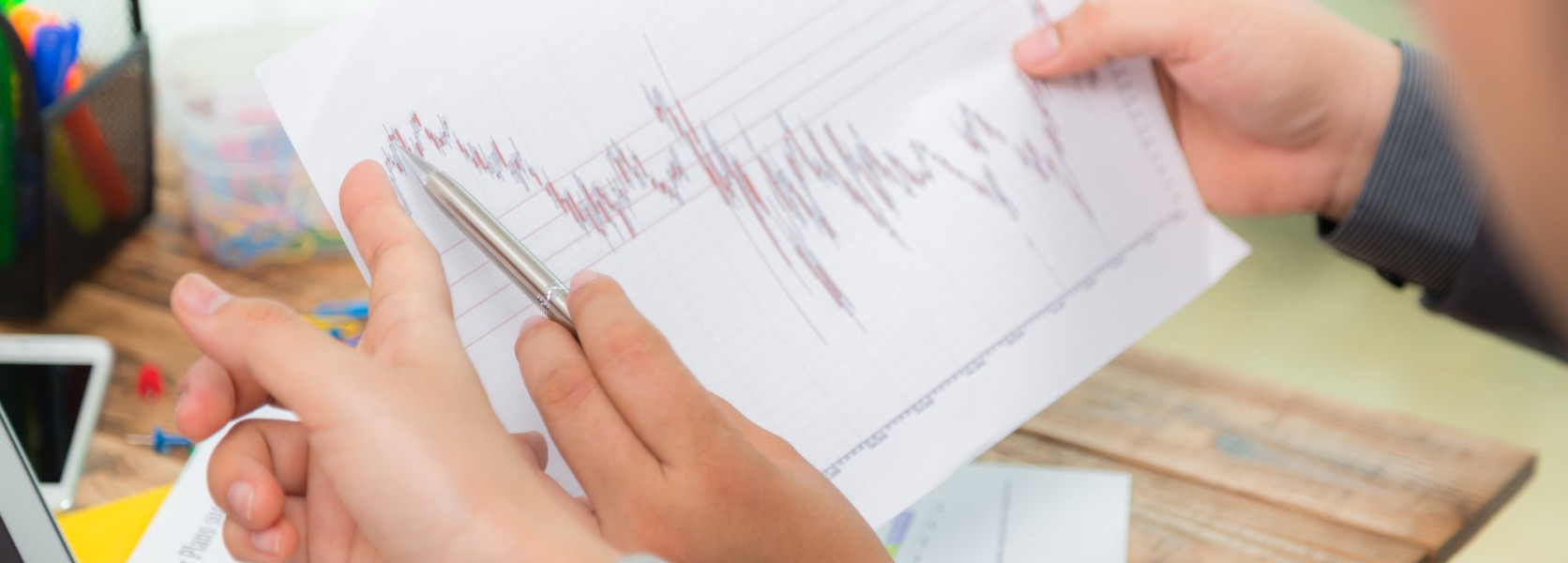 Hands holding a stock chart over a laptop, preparing a retirement portfolio defense strategy against recession