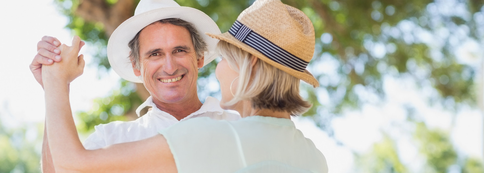 Middle-aged couple dancing outdoors in straw hats, celebrating the financial independence they achieved through FIRE