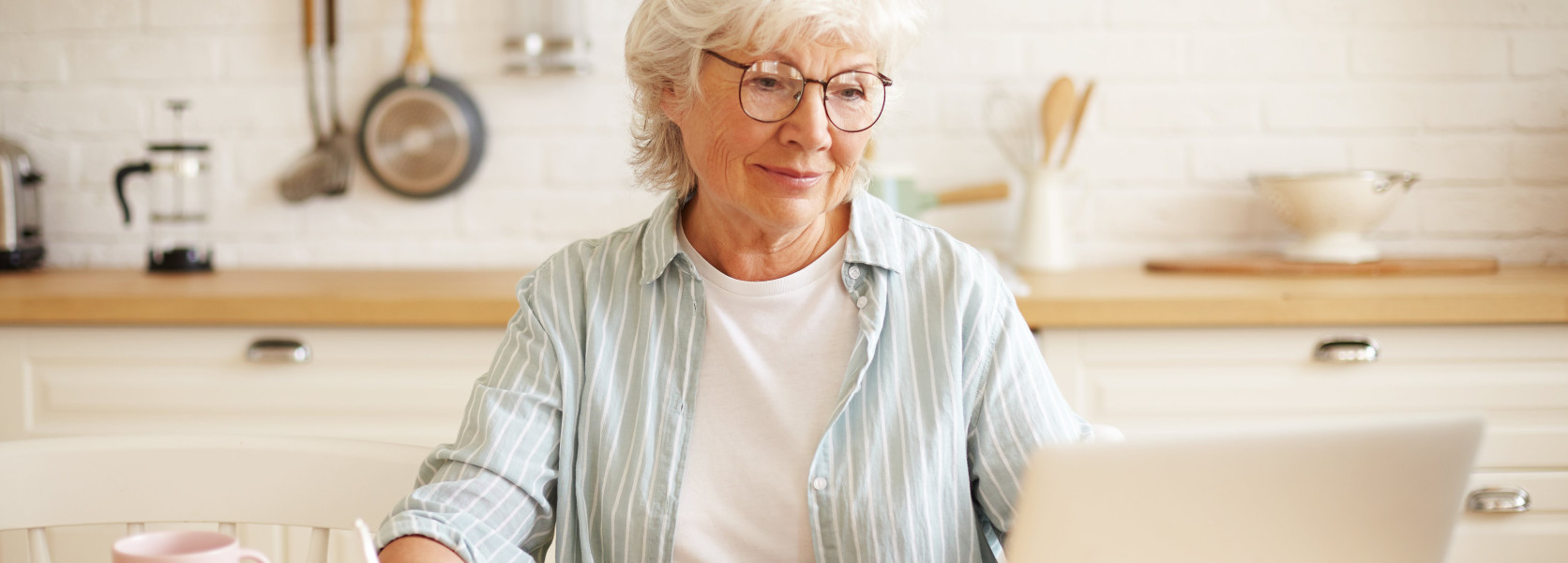 Senior woman writing retirement income notes beside a laptop and calculator at her kitchen table