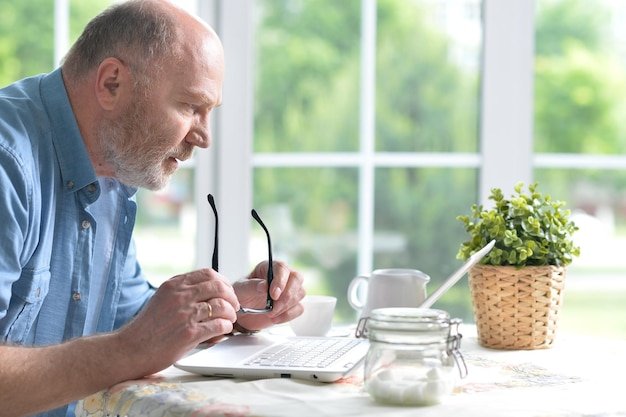 Middle-aged man with glasses reviewing retirement planning documents on a laptop by a bright window