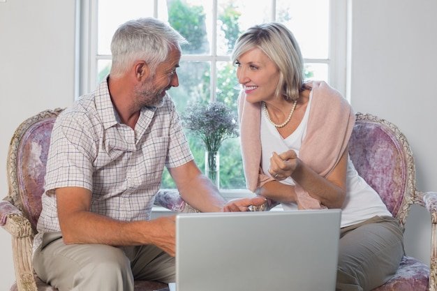 Middle-aged couple on a sofa discussing retirement goals together while looking at a laptop screen
