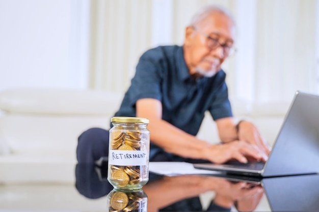 Elderly man at a laptop beside a jar of retirement coins, managing the cash portion of his retirement portfolio