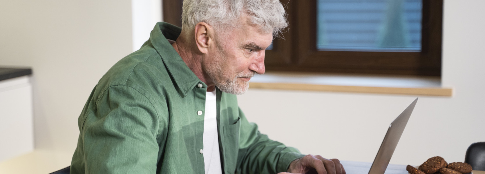 Older man working on a laptop at a kitchen table, carefully rolling over a 401k without triggering tax penalties