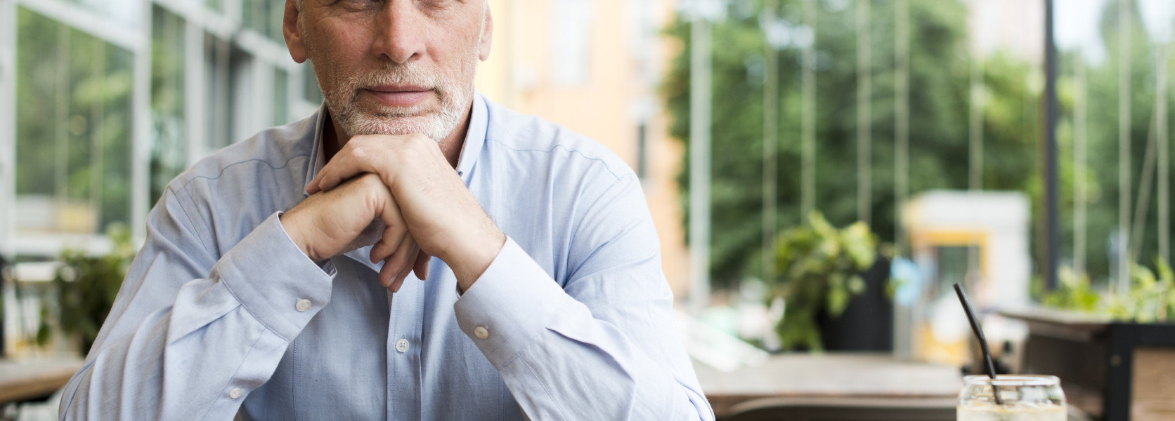 Thoughtful senior man sitting at an outdoor cafe table with a juice, contemplating whether he is ready to retire early