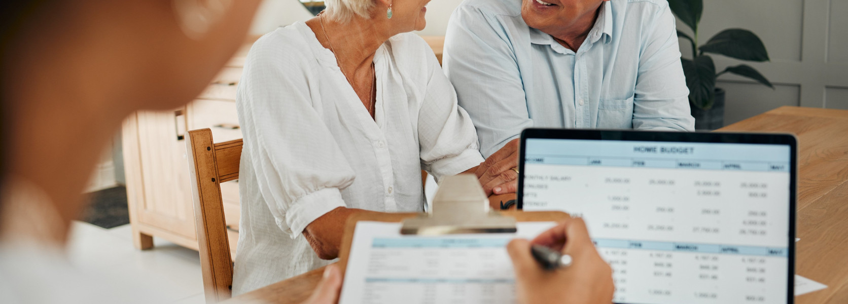 Older couple smiling at a financial review with an advisor and a budget spreadsheet, showing signs of retirement readiness