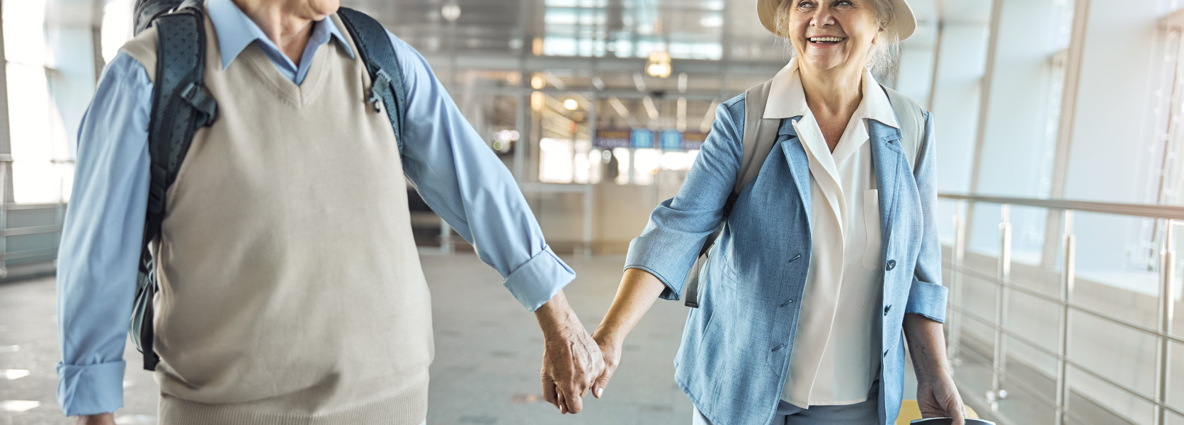 Senior couple holding hands walking through an airport terminal with luggage, exploring how moving abroad affects Social Security